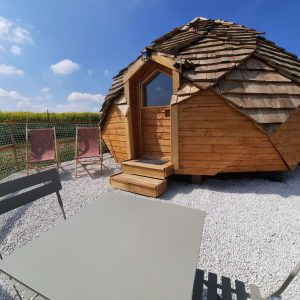 Hébergement insolite en forme de dôme en bois, entouré de verdure et de mobilier extérieur.