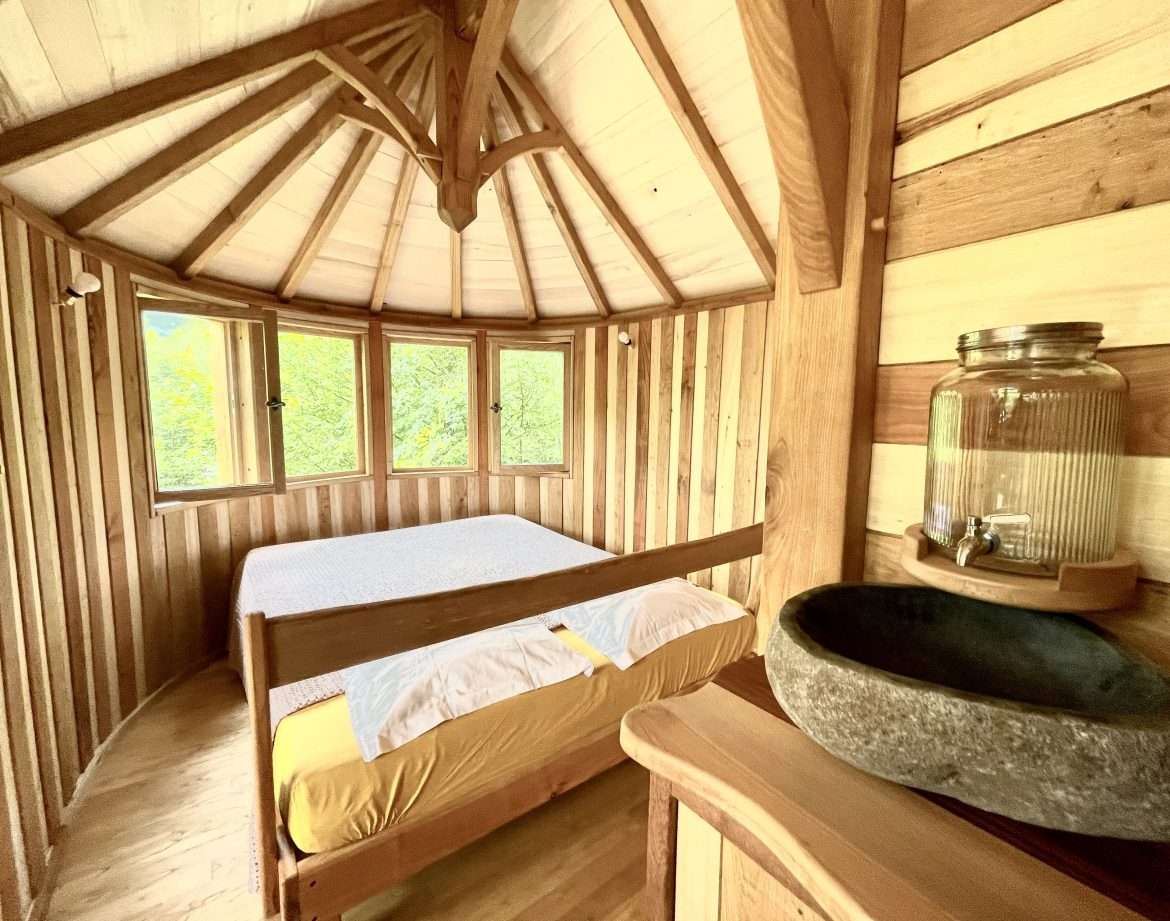 Cabane en bois ronde avec lit douillet et vue sur la nature environnante.