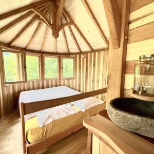Cabane en bois ronde avec lit douillet et vue sur la nature environnante.