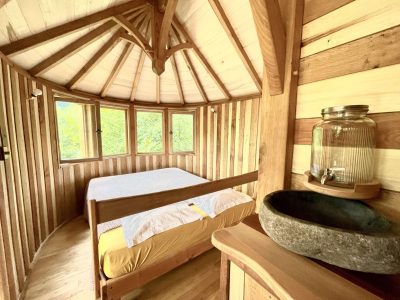 Cabane en bois ronde avec lit douillet et vue sur la nature environnante.