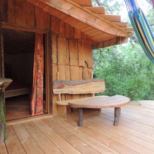 Cabane perchée en bois avec hamacs, offrant une vue sur la nature verdoyante.