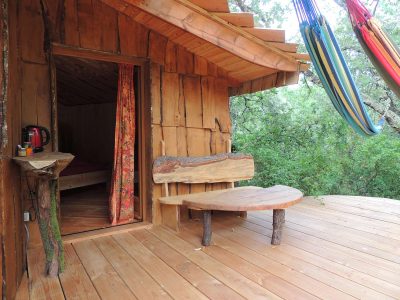 Cabane perchée en bois avec hamacs, offrant une vue sur la nature verdoyante.
