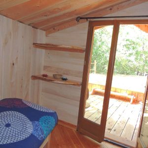 Chalet en bois avec lit coloré et accès à une terrasse ensoleillée.
