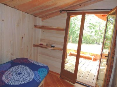 Chalet en bois avec lit coloré et accès à une terrasse ensoleillée.