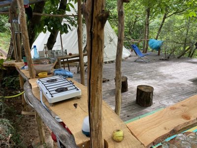 Tente suspendue en pleine nature, avec cuisine en bois et coin détente.