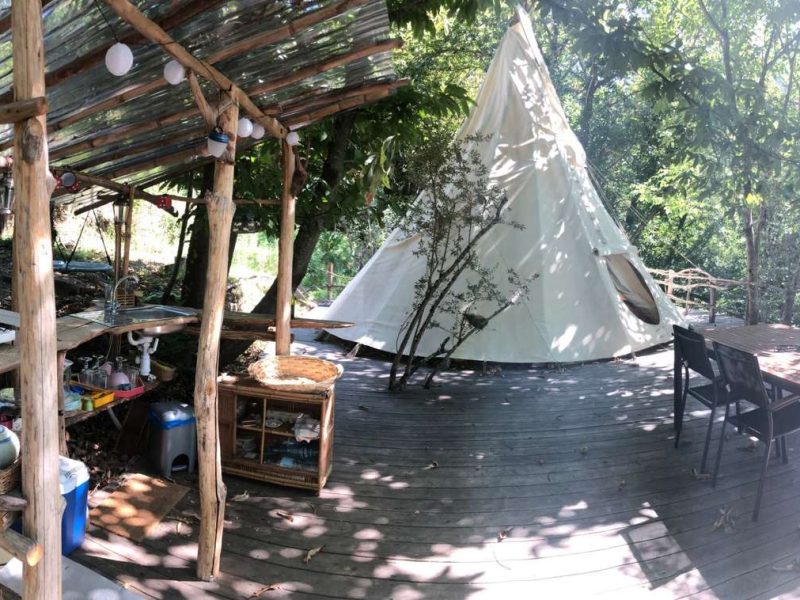 Tente tipi au milieu de la nature, avec une terrasse en bois et un coin cuisine.