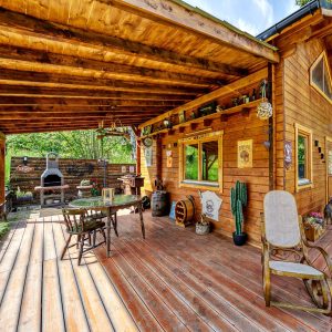 Cabane en bois avec terrasse ensoleillée et coin barbecue, idéale pour se détendre.
