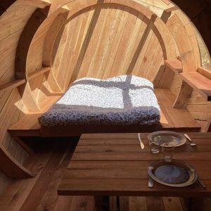Hébergement insolite en forme de tonneau, intérieur en bois avec lit douillet.