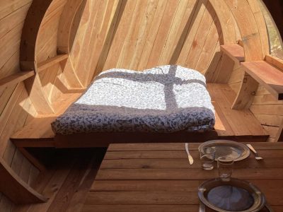 Hébergement insolite en forme de tonneau, intérieur en bois avec lit douillet.