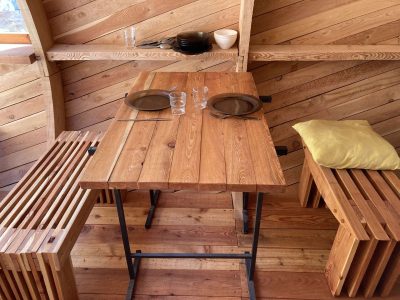 Hébergement insolite en bois avec table et bancs, ambiance chaleureuse et naturelle.