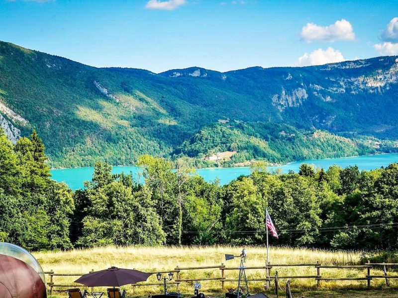 Hébergement en pleine nature avec vue sur un lac turquoise et montagnes verdoyantes.