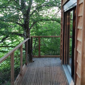 Cabane perchée en bois avec terrasse en bois, entourée de verdure luxuriante.