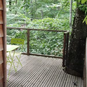 Cabane perchée en bois avec terrasse, entourée de verdure luxuriante.