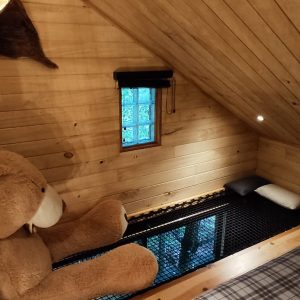 Cabane en bois avec un grand ours en peluche et une fenêtre lumineuse.