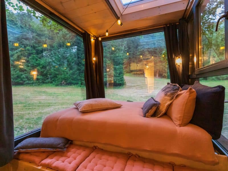 Cabane moderne avec lit douillet et grandes fenêtres sur la nature environnante.
