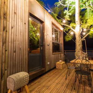 Cabane perchée en bois avec terrasse illuminée par des guirlandes, Auvergne-Rhône-Alpes.