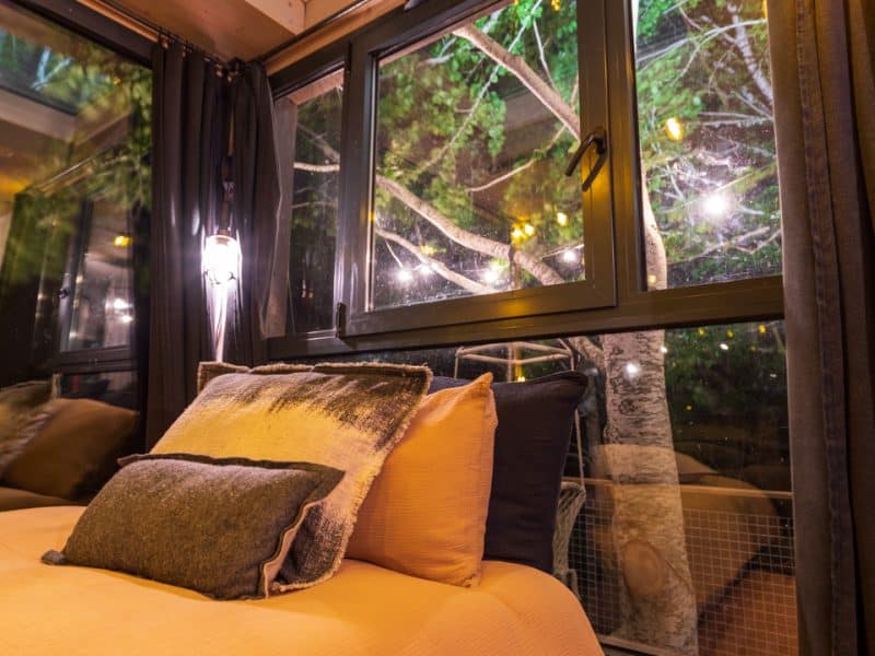Chalet moderne avec lit douillet et vue sur la nature illuminée par des guirlandes.