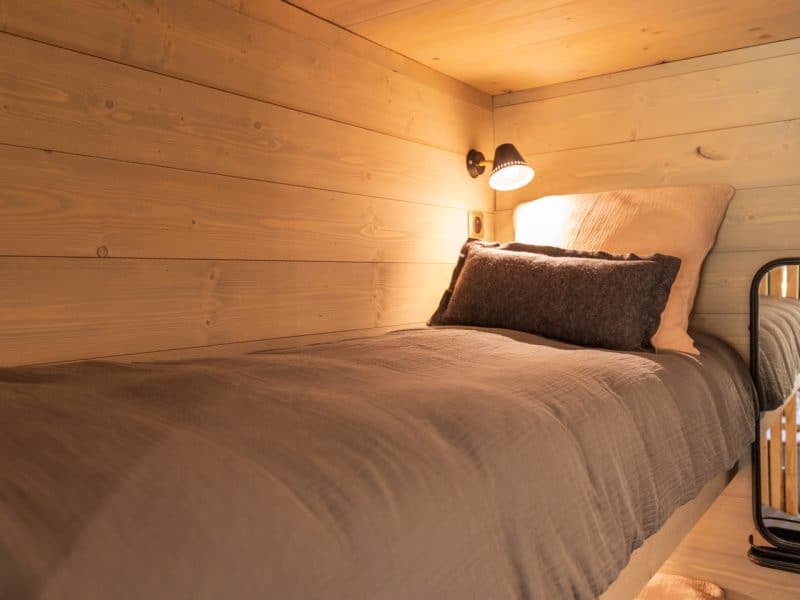 Cabane en bois avec lit confortable et lumière douce, ambiance chaleureuse.