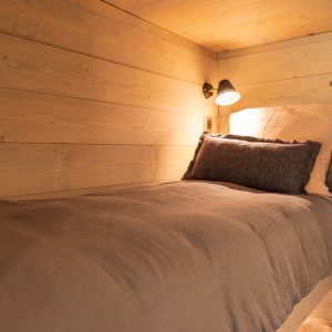 Cabane en bois cosy avec lit douillet et lumière douce, idéale pour un séjour relaxant.