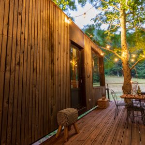 Cabane en bois avec terrasse, éclairage chaleureux et vue sur la nature en Auvergne.