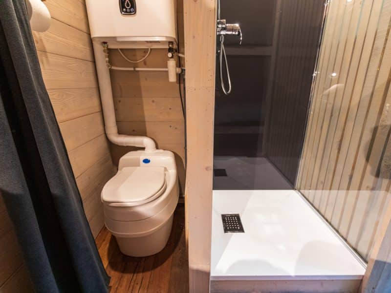 Cabane en bois avec salle de bain moderne, douche spacieuse et toilettes intégrées.