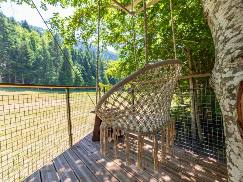 Cabane dans les arbres avec un hamac suspendu, entourée de verdure.