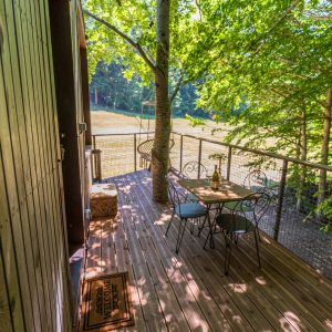 Cabane perchée en bois avec terrasse ombragée et vue sur la nature environnante.