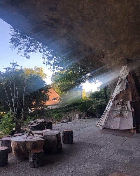 Tipi en pleine nature, éclairé par des rayons de soleil à travers les arbres.