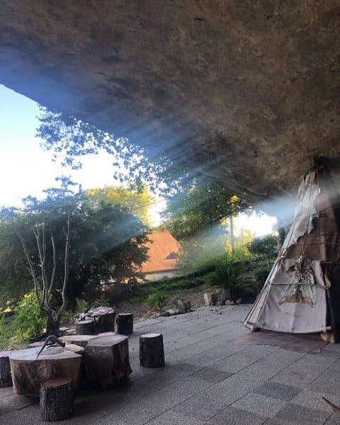 Tente de style tipie sous un rocher, éclairée par des rayons de soleil.