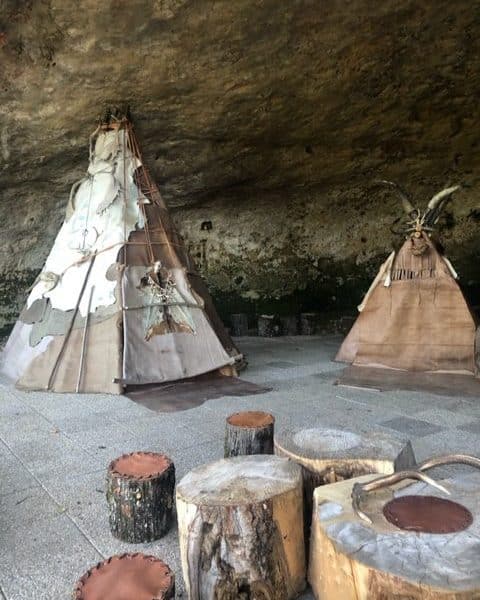 Tentes traditionnelles sous une roche, avec bancs en rondins de bois.