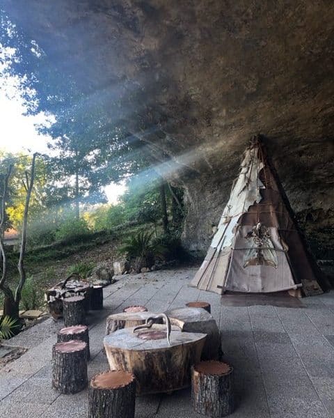 Tente tipi en pleine nature, avec des rondins de bois pour sasseoir.