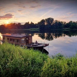 Bateau-hôtel sur la Loire, au coucher de soleil, entouré de verdure paisible.