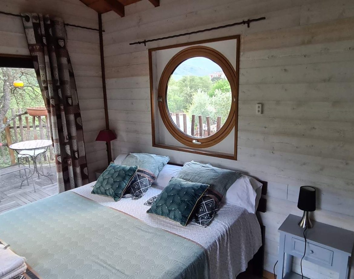 Chalet en bois avec vue sur la nature, lit double et fenêtre ronde.