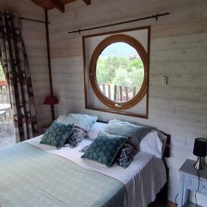 Chalet en bois avec vue sur la nature, lit double et fenêtre ronde.