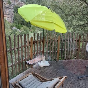 Hébergement insolite en Corse : terrasse en bois avec un transat et un parasol vert.
