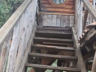 Cabane perchée en Corse, accès par un escalier en bois et fenêtre ronde.