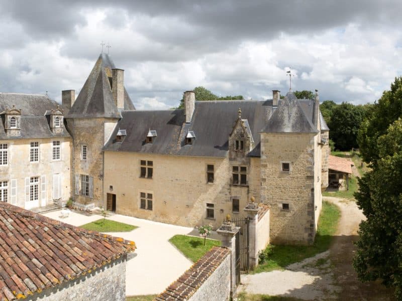 Château historique avec tours, entouré de verdure et dun ciel nuageux.