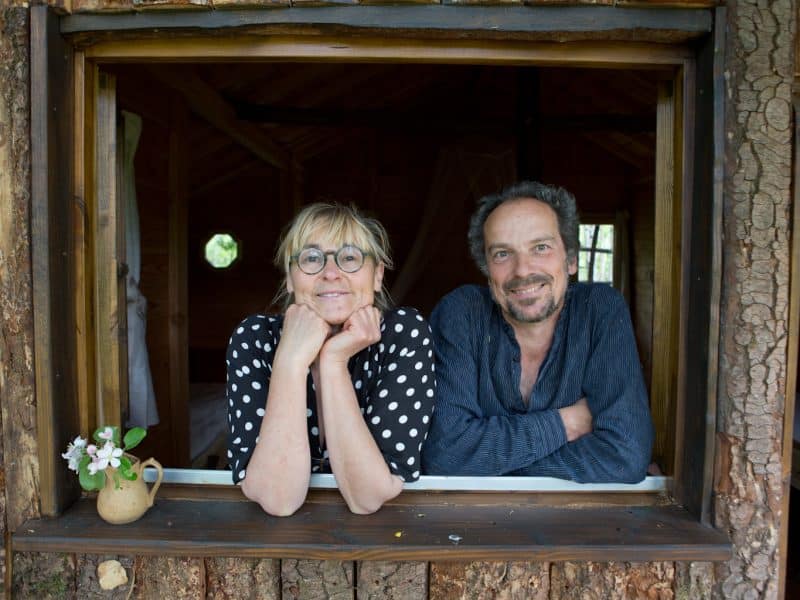 Cabane en bois avec vue sur la nature, accueillie par un couple souriant.