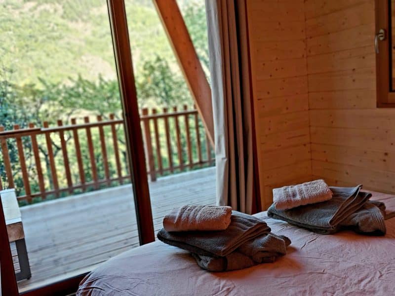 Chalet en bois avec vue sur la nature, linge de lit soigneusement plié.
