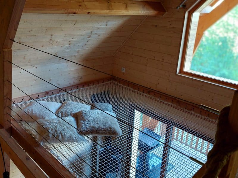 Chalet en bois avec mezzanine, décoré de coussins douillets et lumière naturelle.