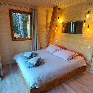 Chalet en bois lumineux avec lit douillet et grandes fenêtres sur la nature.