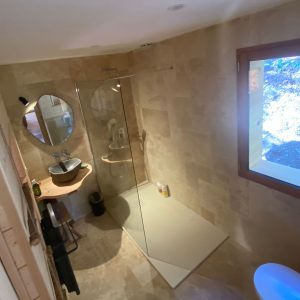 Salle de bain moderne dun hébergement insolite en Provence, avec douche en verre et fenêtre.