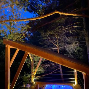 Cabane perchée en bois avec jacuzzi lumineux sous les arbres, ambiance nocturne.