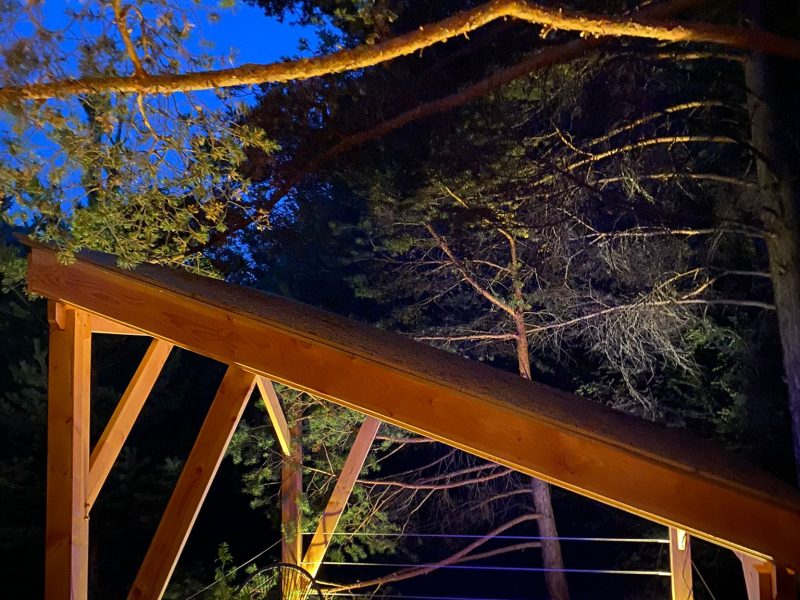 Cabane en bois avec jacuzzi illuminé, nichée sous les arbres au crépuscule.