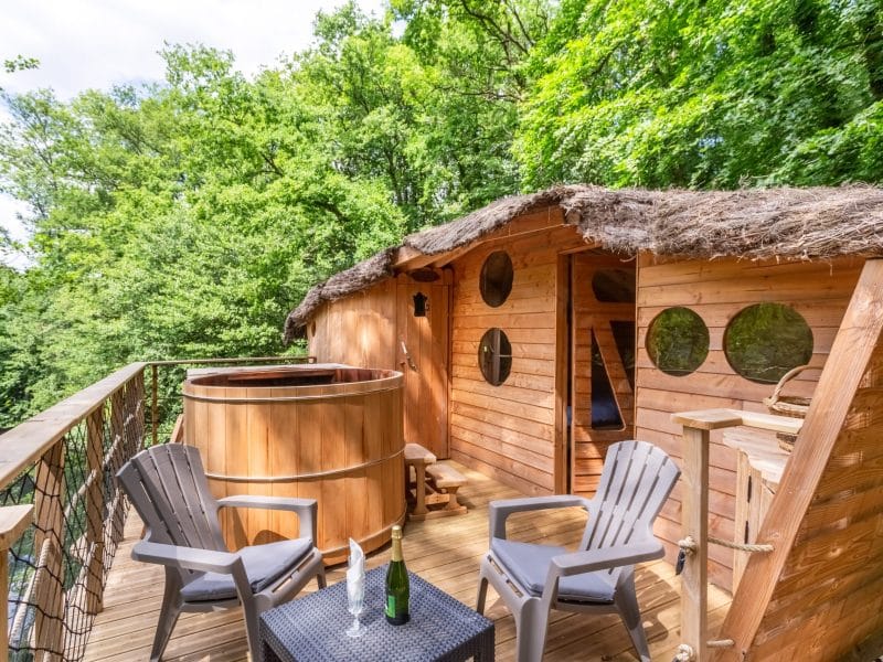 Cabane en bois avec jacuzzi extérieur, entourée de verdure luxuriante.