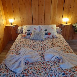 Chambre douillette en bois avec lit floral et serviettes pliées en forme de cœur.