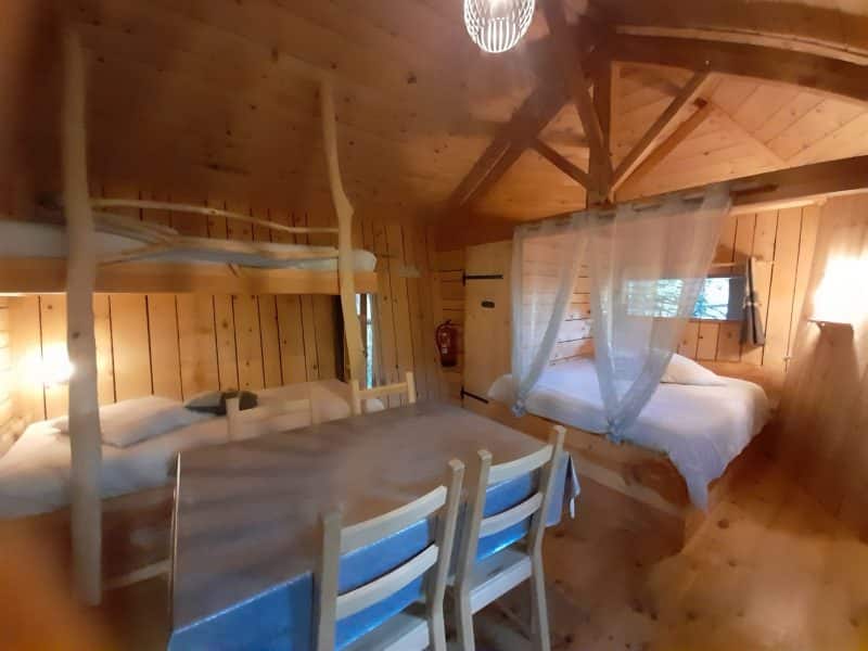 Cabane en bois chaleureuse avec lits superposés et table en bois. Ambiance cosy.