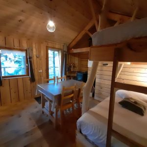 Cabane en bois chaleureuse avec lit superposé et table en bois, au cœur de la nature.