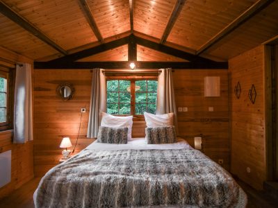 Chalet en bois chaleureux avec lit douillet et lumières tamisées.