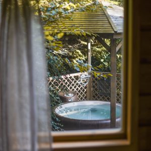 Cabane en bois avec vue sur un jacuzzi extérieur entouré de verdure.